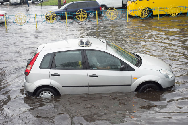 Θεματική εικόνα για: «νερό στον κινητήρα του αυτοκινήτου». Γκρι αμάξι είναι ακινητοποιημένο σε πλημμυρισμένο δρόμο.