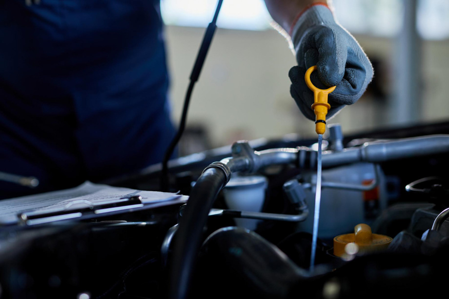 Μηχανικός σε συνεργείο ελέγχει τα λάδια ενός αυτοκινήτου με ειδικό εργαλείο και φορώντας γάντια.