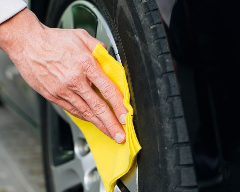 Άτομο σκουπίζει τις ζάντες αλουμινίου του αυτοκινήτου του με κίτρινο πανί.