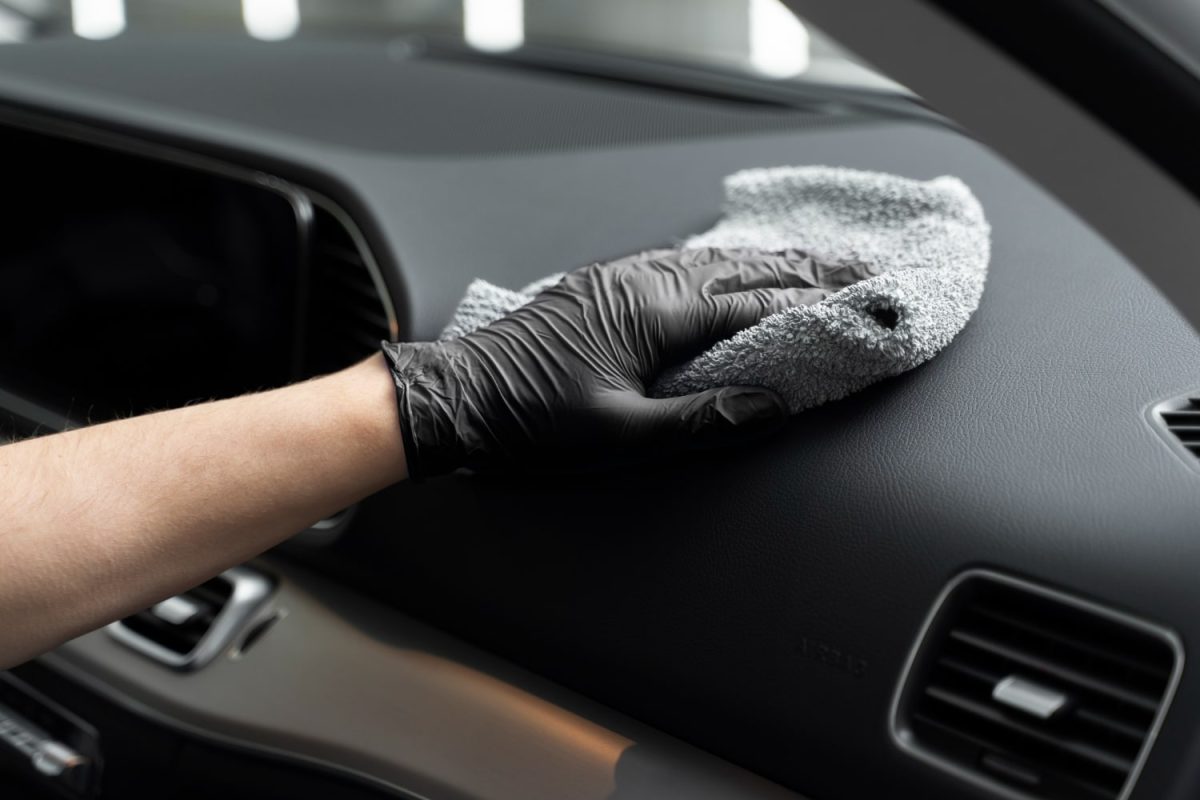 Συντήρηση πλαστικών αυτοκινήτου. Άντρας με μαύρο γάντι καθαρίζει με πανάκι το ταμπλό του αμαξιού του.